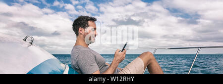 Yacht de luxe young man using cellphone banner panorama. Personne relaxing on deck sms message sms sur téléphone mobile sous le soleil d'été. Banque D'Images