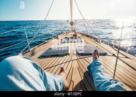 Bonheur et détente concept pour traveler personnes - homme jambes point de vue sur un voilier en bois avec soleil et autour de l'océan bleu - Luxe et maison de vac Banque D'Images