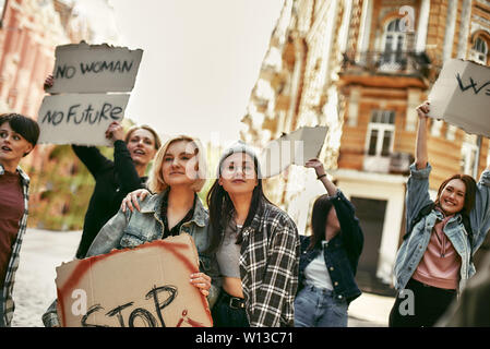 Deux jeunes et heureux les femmes dans des vêtements décontractés sont tenant une bannière avec mention stop en étant debout sur la route dans le groupe de femmes activistes. Banque D'Images