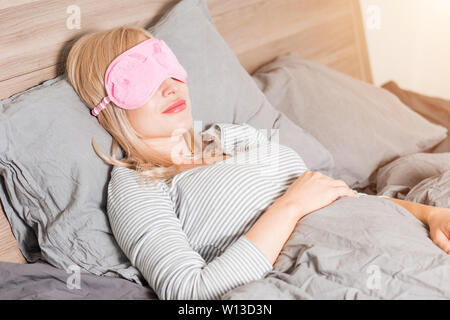 Young blonde woman sleeping in bed. Libre passage portrait de belles femmes portant des pyjamas rayés en appui sur le lit confortable, allongé sur gris pi Banque D'Images