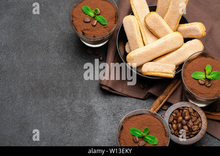 Cadre fait de dessert tiramisu classique dans un verre et savoiardi cookies sur fond de béton foncé Banque D'Images