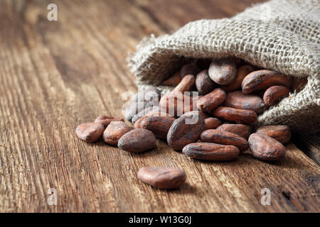 Fèves de cacao dans un sac sac sur un fond de bois. Banque D'Images