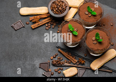 Cadre fait de dessert tiramisu classique dans un verre et savoiardi cookies sur fond de béton foncé Banque D'Images