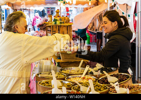 Marché de l'olive française stall en anglais town square avec de l'argent pour payer des mâles matures femme titulaire de décrochage. Différents types d'olives sur l'affichage dans des conteneurs. Banque D'Images