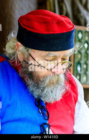 Reconstitution médiévale événement. Close up of senior man de visage, tôlier, avec barbe touffue, le port de lunettes, médiévale et tambourin hat. Banque D'Images