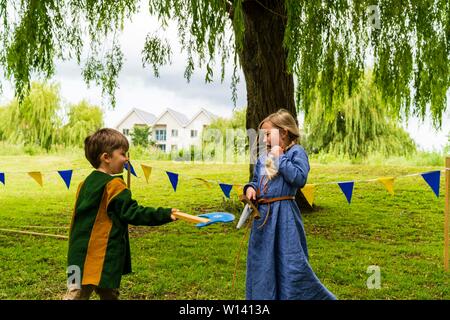 Deux enfants, garçon, 4-5 ans, et une fille, 5-6 ans, vêtu de vêtements médiévaux et les combats de manière ludique à l'épée et hache sur l'herbe. Banque D'Images