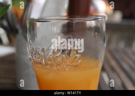 Close up of Coca Cola en verre avec du jus d'orange, dans un jardin de bière sur une table brune sur une journée ensoleillée Banque D'Images