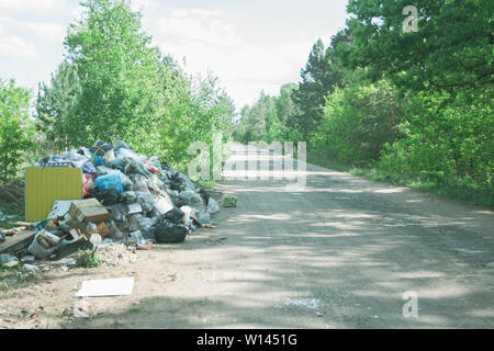 Décharge illégale près de la route de sable de pays dans le pays le jour de soleil. Corbeille de la pollution dans la nature. Dirty dépotoir près de tons bois forêt Banque D'Images