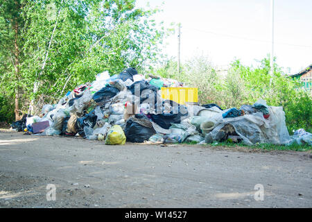 Décharge illégale près de la route de sable de pays dans le pays. Ensoleillé. Corbeille de la pollution dans la nature. Dirty dépotoir près de bois de la forêt Banque D'Images