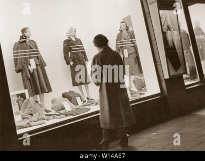 Faire du lèche-vitrine dans les années 1950. Une femme se tient debout à l'extérieur d'une fenêtre d'affichage de la boutique avec les derniers womens fashion. Les mannequins portent les saisons automne et hiver. Suède 1951 Banque D'Images