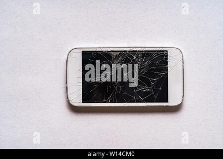 Broken téléphone mobile avec écran fissuré sur fond gris, mise à plat. Banque D'Images