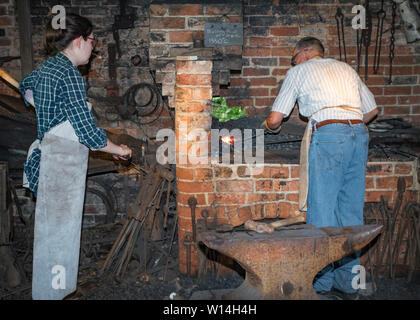 Un forgeron de sexe masculin travaillant dans une forge avec une femme pompe le soufflet. Banque D'Images