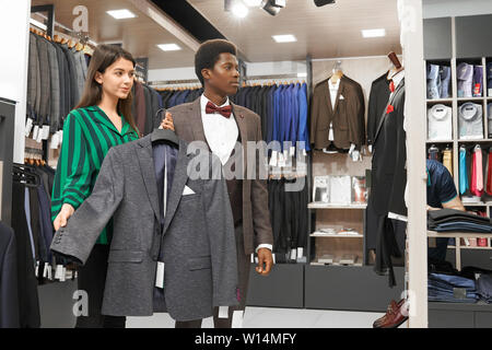 Beau client, en Afrique de l'enveloppe du costume élégant choix boutique. Jolie veste assistant portant sur le crochet. L'homme et à l'écart, consultant boutique Banque D'Images