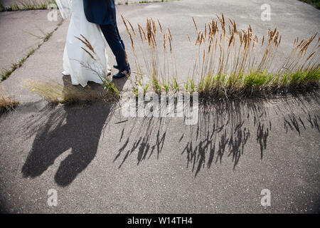 Les jambes de l'époux en bleu chaussures et des pantalons et des épouses en robe de mariage blanc comme neige.L'ombre de la mariée et le marié sur la chaussée Banque D'Images