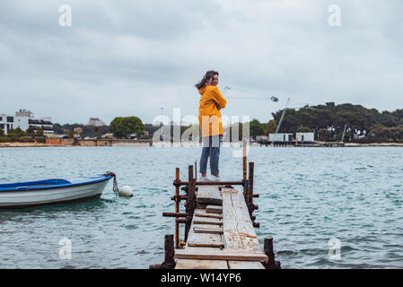 Femme debout sur le bord de la petite jetée de pêche à la mer à l'assaut par temps couvert. Banque D'Images