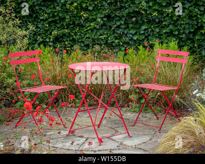 De jardin avec petite terrasse et deux chaises rouges avec table en métal entouré de fleurs d'été et les herbes. Banque D'Images