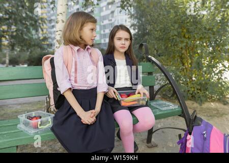 Portrait d'automne d'enfants ayant des boîtes à lunch, les sacs à dos de l'école. Cheerful écoliers mangent des fruits, à rire, à parler. Des aliments sains et en bonne santé lifesty Banque D'Images