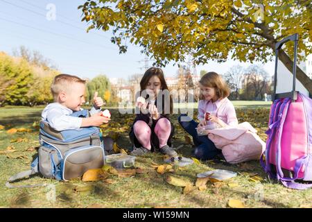 Portrait d'automne d'enfants ayant des boîtes à lunch, les sacs à dos de l'école. Cheerful écoliers mangent des fruits, à rire, à parler. Des aliments sains et en bonne santé lifesty Banque D'Images