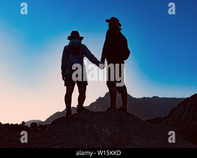 Heureux couple sur le sommet de la montagne et de regarder à vue à couper le souffle au coucher du soleil Banque D'Images