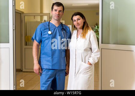 Portrait de couple dans l'âge moyen, blanc caucasien, médecins, hommes et femmes en robe blanche et bleu des gommages corporels avec stéthoscope, couloir de l'hôpital je floue Banque D'Images