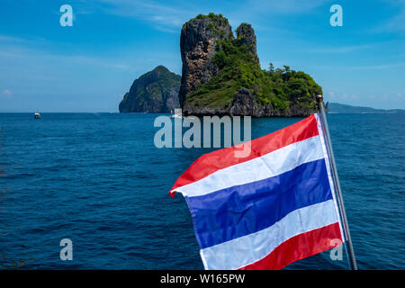 Un paysage marin d'une petite île thaïlandaise de calcaire dans les eaux scintillantes de la mer d'Andaman, avec le drapeau de la Thaïlande palpitations dans l'avant-plan Banque D'Images