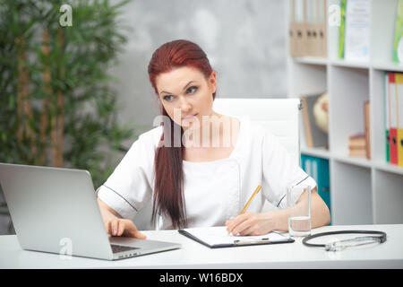Certain femme médecin assis à la table dans son bureau et travaille à l'ordinateur. concept de soins de santé. Banque D'Images