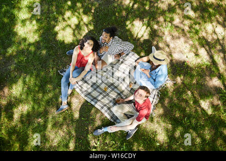 Voir ci-dessus portrait de groupe d'amis profiter de pique-nique sur l'herbe verte en été et à la recherche jusqu'à l'appareil photo, copy space Banque D'Images