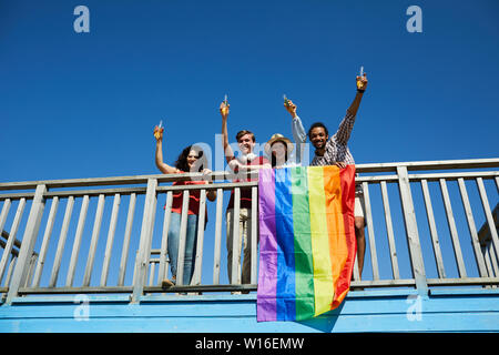Low angle portrait of happy young people standing on bridge et acclamer avec drapeau arc-en-ciel en premier plan, copy space Banque D'Images