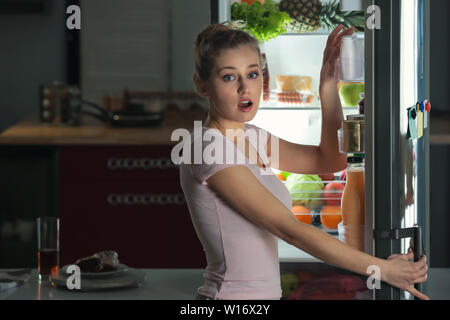 Peur femme prise dans le fait de choisir une cuisine savoureuse au réfrigérateur pendant la nuit Banque D'Images