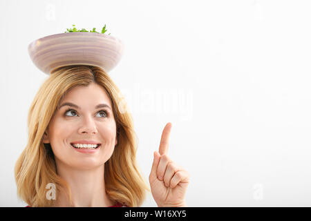 Femme avec bol de salade de légumes sains sur la tête du doigt quelque chose contre l'arrière-plan clair Banque D'Images