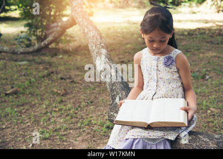 Cute girl reading a book in the park. Dur apprentissage de l'élève en dehors de l'école. Banque D'Images