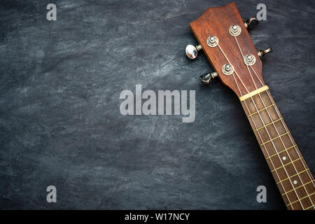 Ukulele sur fond de ciment noir. Poupée et fret de ukulele pièces. L'espace de copie pour le texte. Concept d'instruments de musique hawaïenne et les amateurs de musique Banque D'Images