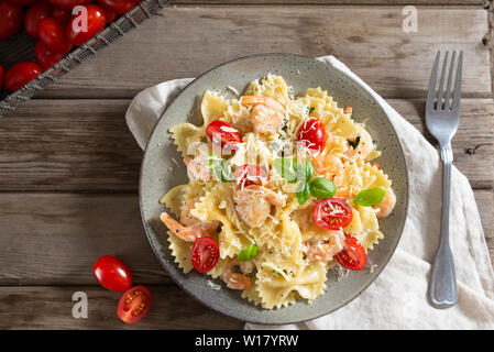 Farfalle pâtes italiennes dans une sauce crémeuse aux crevettes sauce à l'ail, tomates cerises et basilic sur une assiette, vue d'en haut. Copy space Banque D'Images