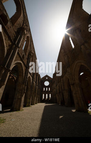 La nef centrale de l'abbaye sans toit de San Galgano, lors d'une journée ensoleillée avec sun flare sur un côté. Chiusdino, Italie. Prise de vue au grand angle vertical. Banque D'Images