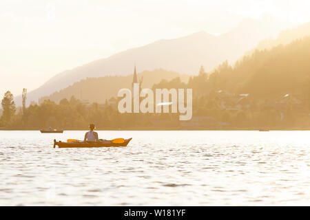Femme kayak au coucher du soleil dans le lac Weissensee, Autriche Banque D'Images