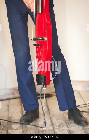 La musique de fond, l'homme joue de la contrebasse électrique moderne rouge en studio de musique, photo en gros plan avec selective focus Banque D'Images