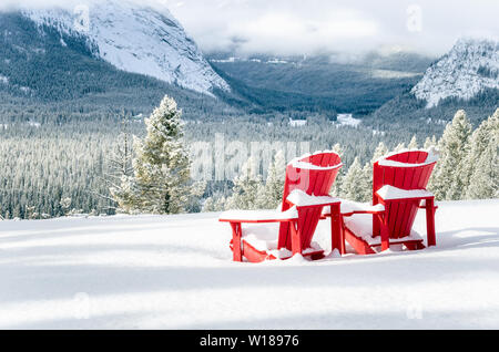 Couvert de neige des chaises Adirondack rouge face à une vallée boisée sur une journée d'hiver. Le parc national Banff, AB, Canada. Banque D'Images