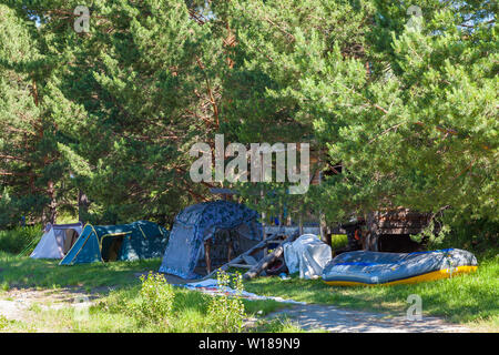 Camping tente à l'ombre sous les arbres avec une maison en bois et un grand bateau gonflable rafting près de la rivière dans les montagnes de l'Altaï. Sport extrême Banque D'Images