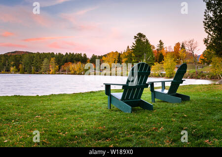Deux chaises Adirondack vide sur une pelouse, face à un lac au crépuscule. Belles couleurs d'automne. Banque D'Images