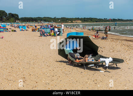 Un avis de voyageurs sur Avon Beach, Mudeford, Christchurch, Dorset, UK avec parasols et de brise-vent. Une plage de sable sur une journée d'été. Banque D'Images