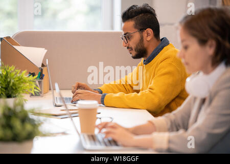 L'accent sur les jeunes sérieux homme moyen-orientale en jaune pour homme assis à table et la préparation de présentation sur ordinateur portable Banque D'Images