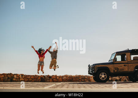 Jeune homme et femme sautant en plein air en face de la voiture. Couple having a great time on road trip. Banque D'Images