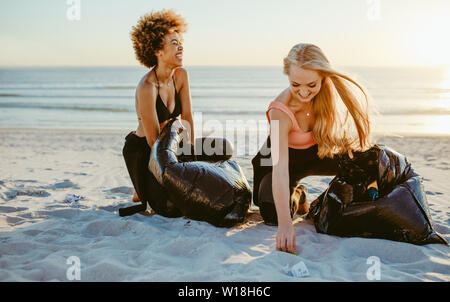 Happy female surfers faire trash tag challenge sur la plage. Les femmes le nettoyage de plage. Banque D'Images