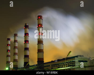 Vue de nuit sur les tuyaux de centrales thermiques, émettant de la fumée dans l'atmosphère de la ville, mis en lumière par en dessous par le rétro-éclairage et un trouble Banque D'Images