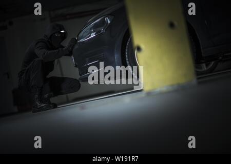 Voleur de voiture essayant d'ouvrir le capot du véhicule pour obtenir l'accès aux système d'alarme. Parking public à la nuit. Grand Theft Auto Thème. Banque D'Images