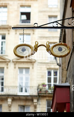 Paire de lunettes cerclées d'or, les yeux bleus - creative design enseigne suspendue au-dessus d'un magasin opticiens dans une rue de Bordeaux Banque D'Images