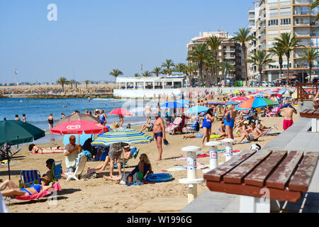 Torrevieja, Espagne - 10 juin 2019 : Beaucoup de touristes profiter de chaude journée d'été dans la plage de sable de Playa Del Cura, les vacanciers à l'ombre des parasols vous détendre Banque D'Images