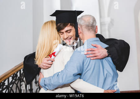 Cheerful fils en graduation cap holding diploma tout en serrant les parents