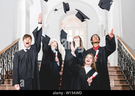 Happy students smiling tout en jetant dans l'obtention du diplôme d'air caps Banque D'Images