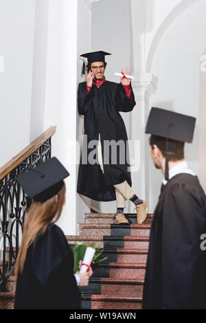 Cheerful man talking on smartphone et forme des étudiants dans l'obtention du diplôme caps Banque D'Images